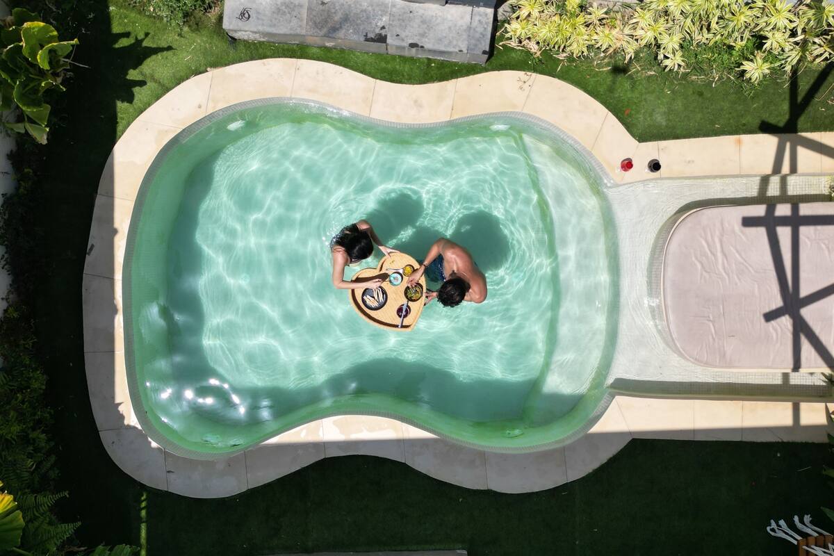 Ein Pool mit ungewöhnlicher Form, umgeben von einer Rasenfläche und Pflanzen.