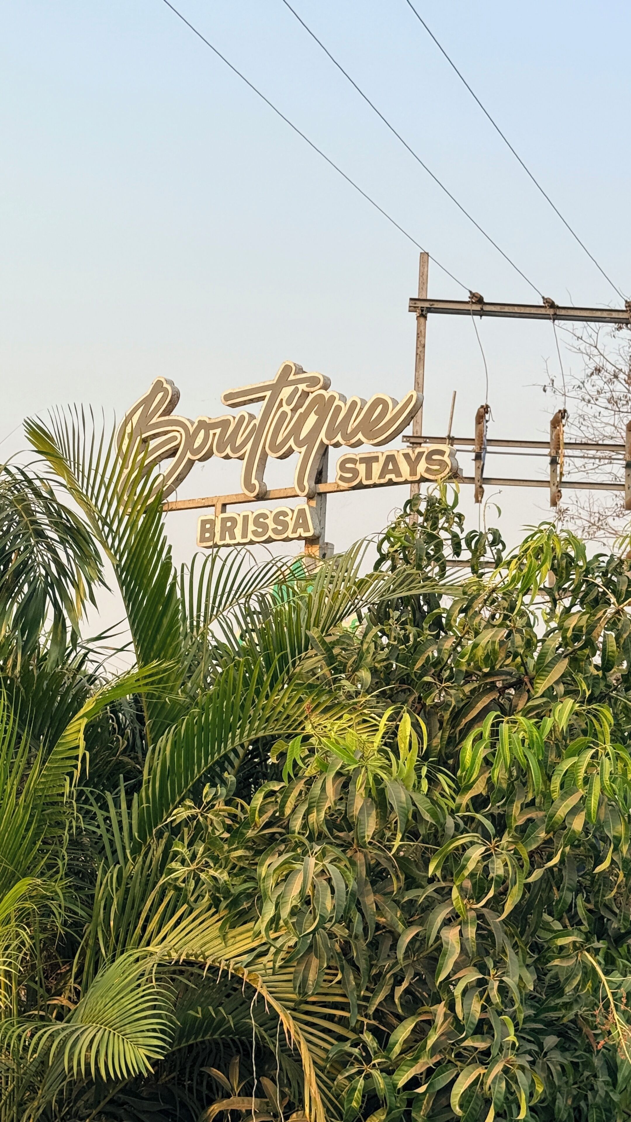 A sign for Boutique Brissa Stays with a backdrop of lush greenery.