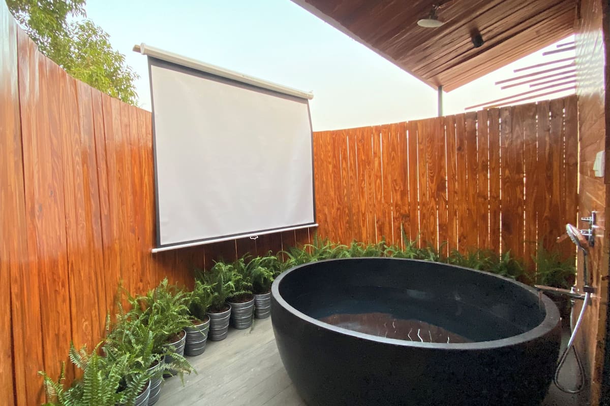 Eine Holzterrasse mit einem schwarzen Whirlpool, einem weißen Sichtschutz und Topfpflanzen.