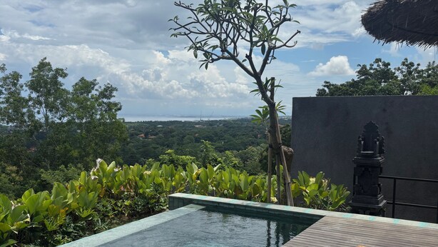 Ein Pool ohne Ende mit Holzterrasse und Liegestühlen, umgeben von üppiger Vegetation und Blick auf die Landschaft.
