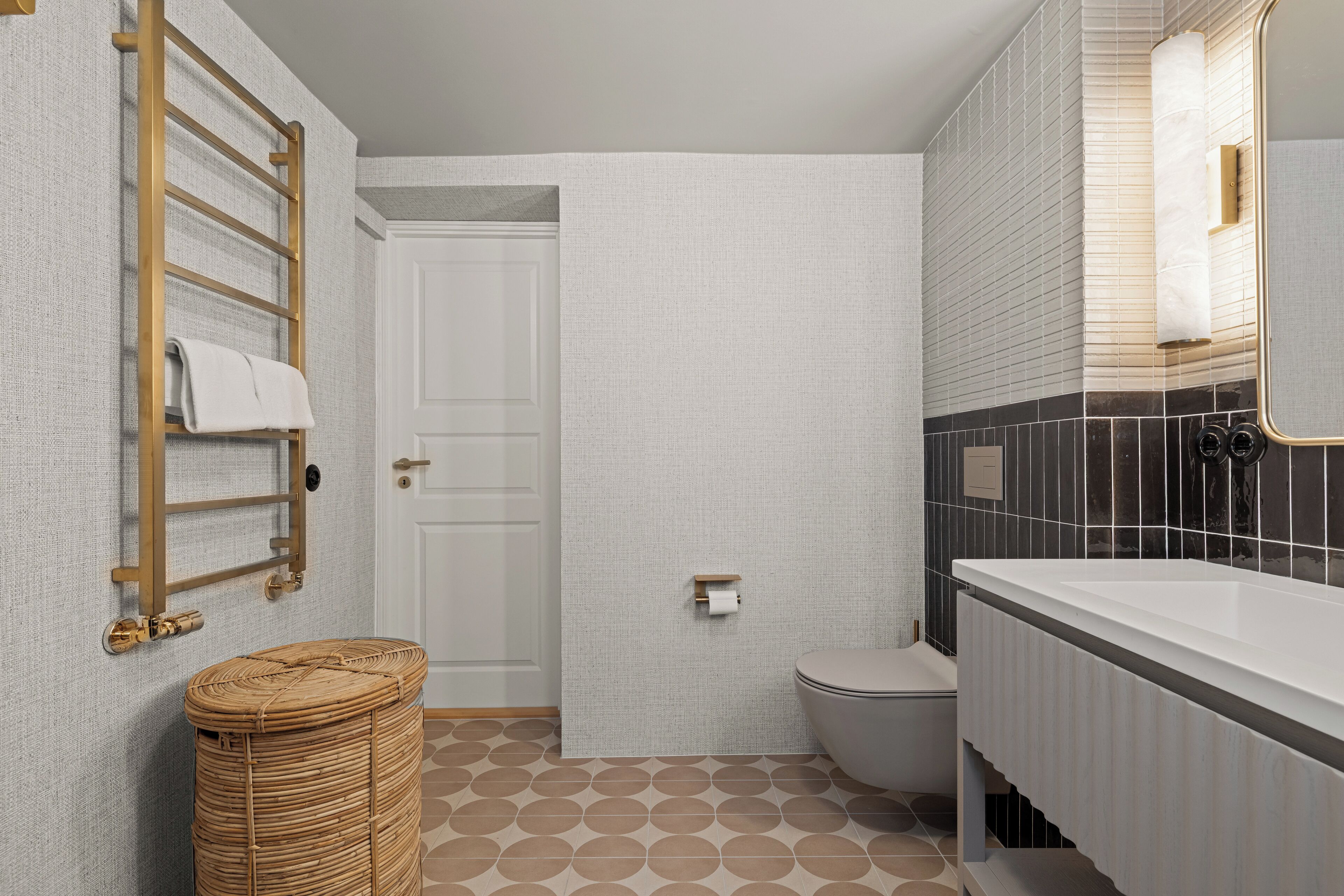 A bathroom with a white door, a toilet, a white sink, a towel rack, and a wicker basket.