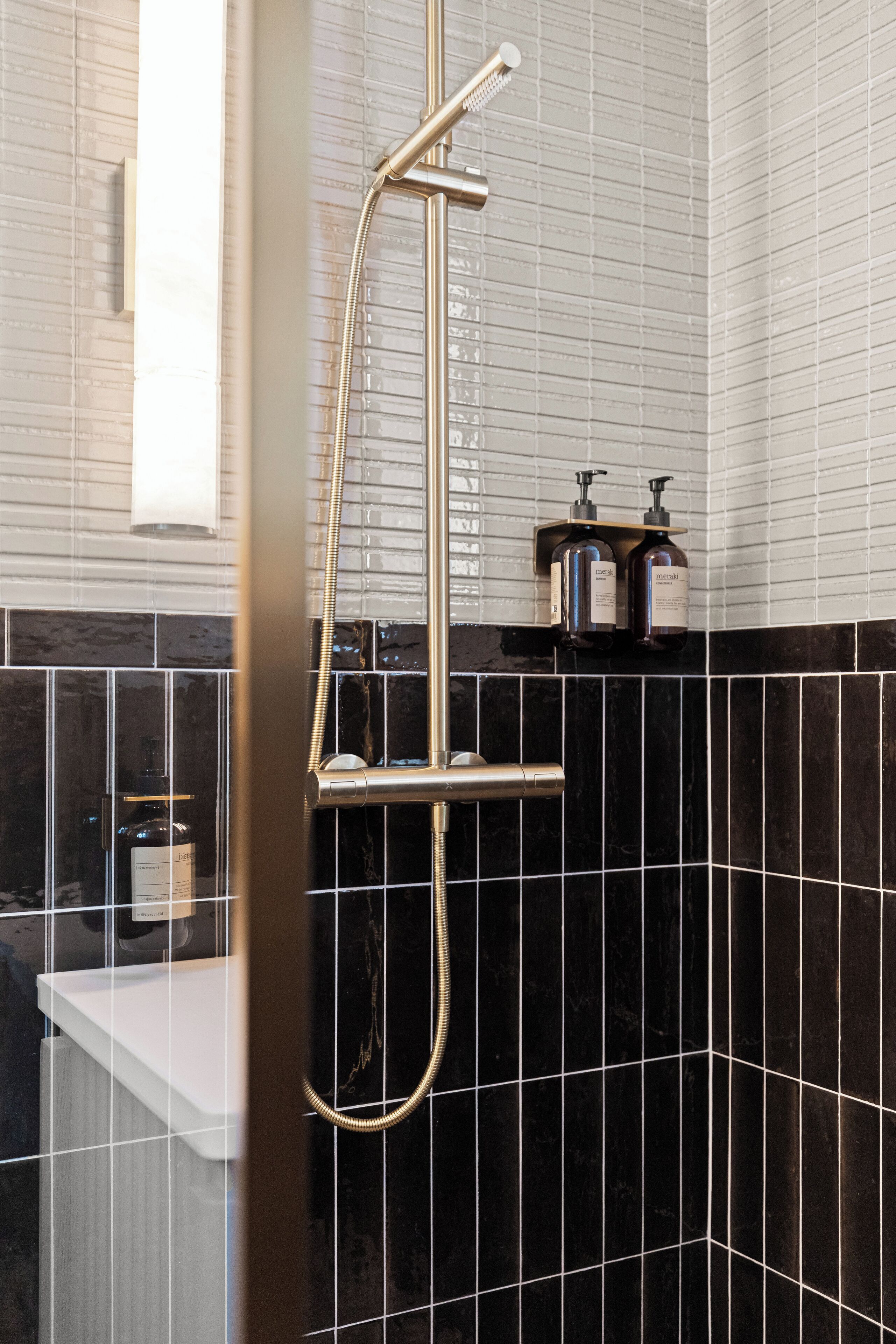 A modern bathroom with a glass-enclosed shower, black and white tiled walls, and a white countertop.