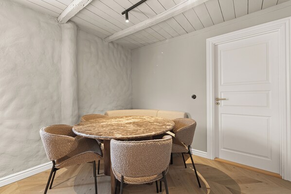 Um quarto com uma mesa redonda de madeira, rodeada por quatro cadeiras de fibra, uma porta branca e uma parede texturizada em branco.