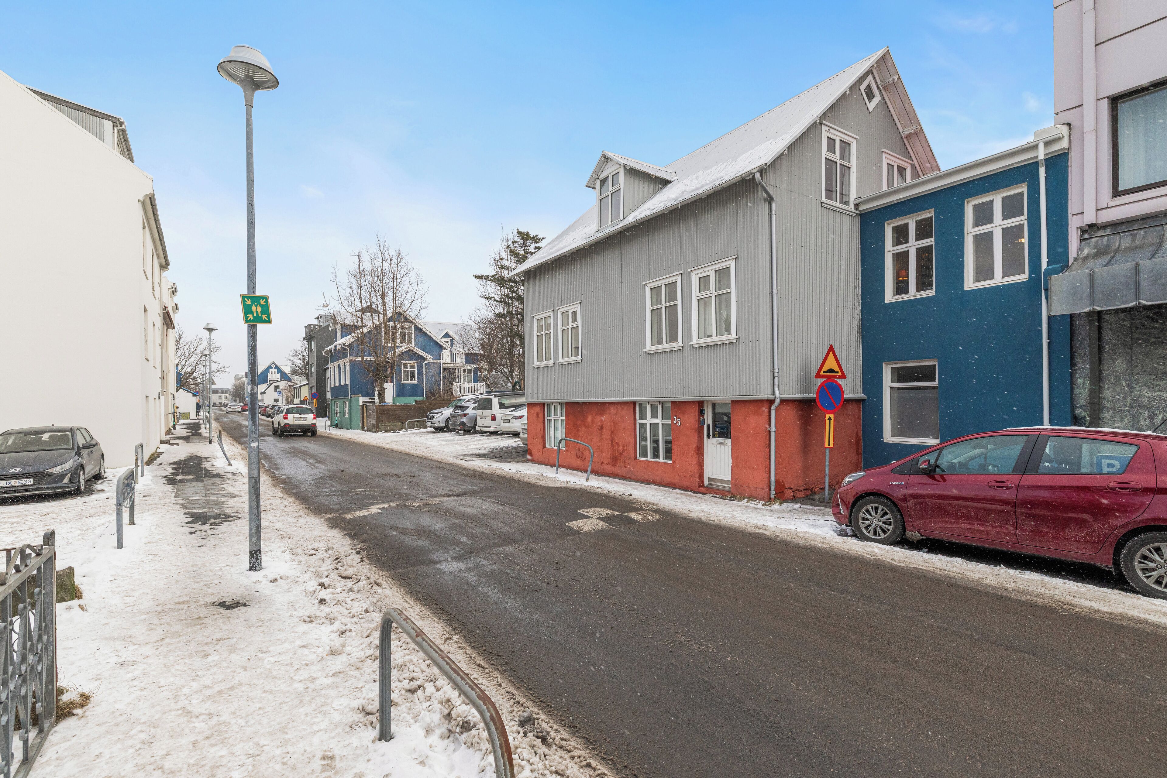 Une rue bordée d’immeubles, une voiture rouge garée sur le côté et un panneau indiquant qu’il est interdit de se garer.