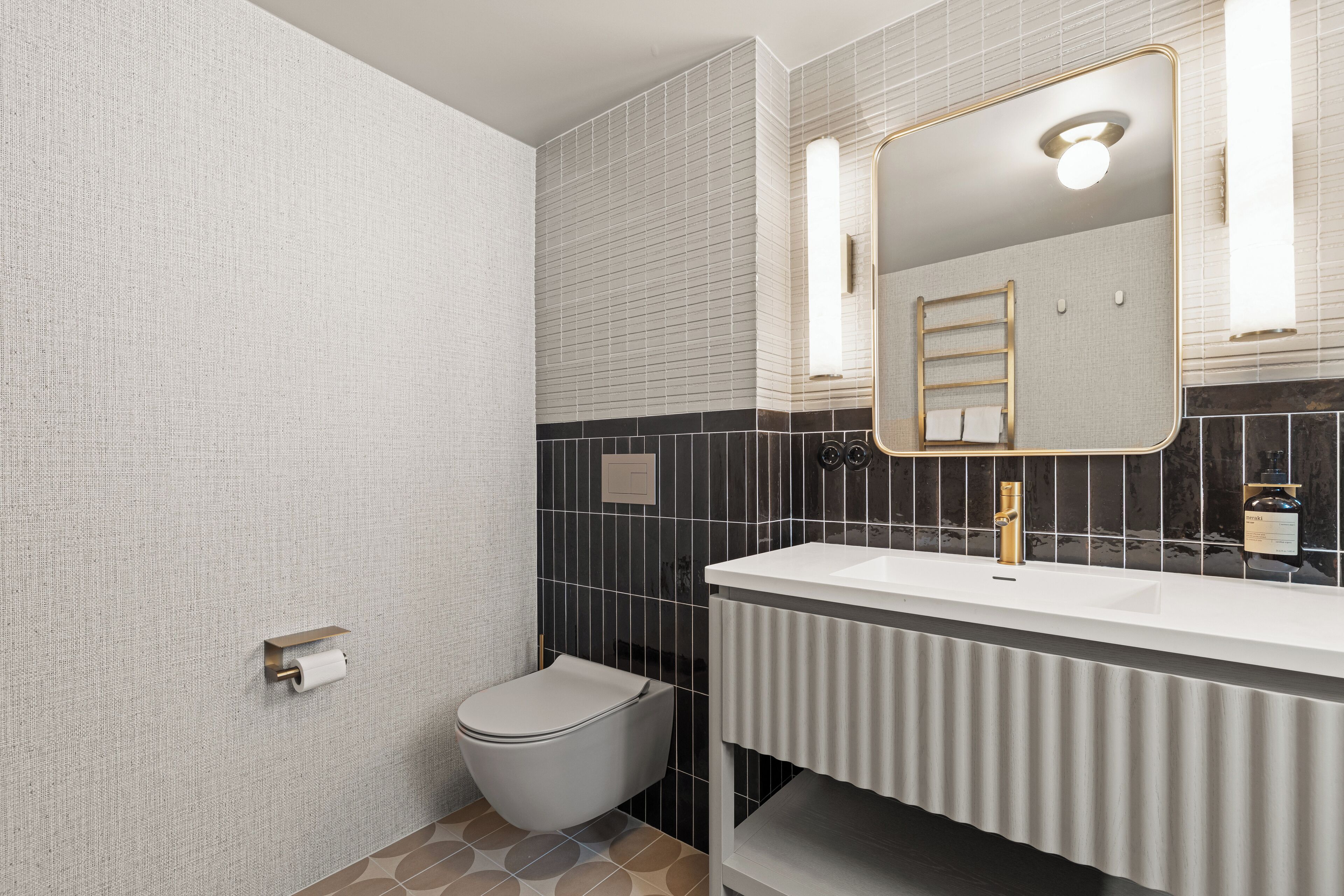 A modern bathroom with a white sink, gold faucet, and a mirror with a gold frame.