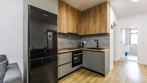 Una cocina compacta con un refrigerador negro, armarios de madera, horno empotrado y un lavamanos.