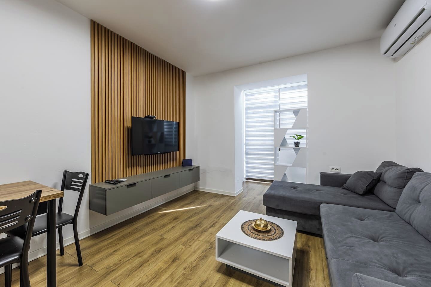 A modern living room with a wooden accent wall, a grey sofa, a white coffee table, and a TV mounted on the wall.