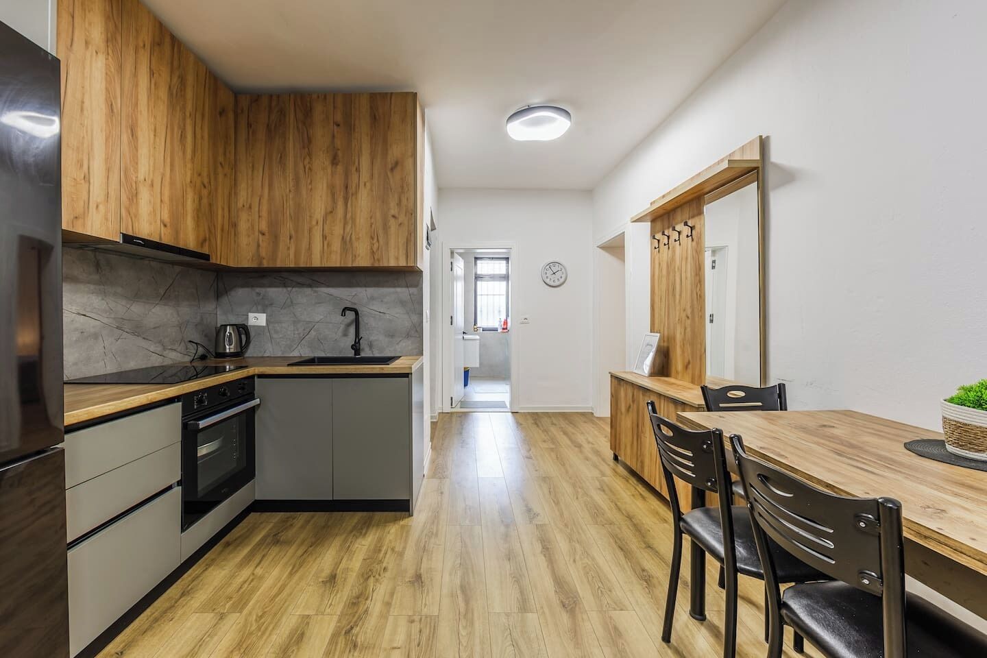 Een moderne keuken met houten kastjes, een ingebouwde oven en een eethoek met een houten tafel en stoelen.