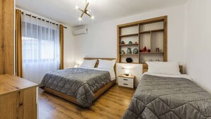 Habitación de hotel con dos camas, piso de madera, lámpara de techo, mesita de noche con lámpara y estante empotrado con adornos.
