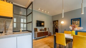 Et moderne køkken med indbygget ovn, et spiseområde med gule stole og et fladskærms-TV på væggen.