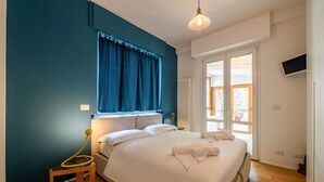 Et soveværelse med en stor seng, et vindue med gardiner, et sengebord med en lampe og et fjernsyn monteret på væggen.