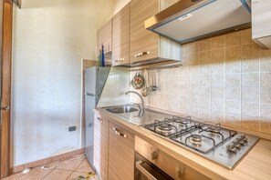 A kitchen with a gas stove, stainless steel sink, wooden cabinets, and a tiled backsplash. - Holiday Home 'Villa Barbara A By Salentolimit' with Private Garden (Porto Cesareo)