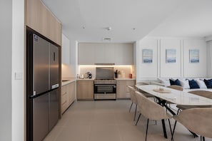 A modern kitchen with a built-in oven, a refrigerator, and a dining area with a table and chairs. - Burj Khalifa Views l Luxury Stay with Pool & Gym (Dubai)