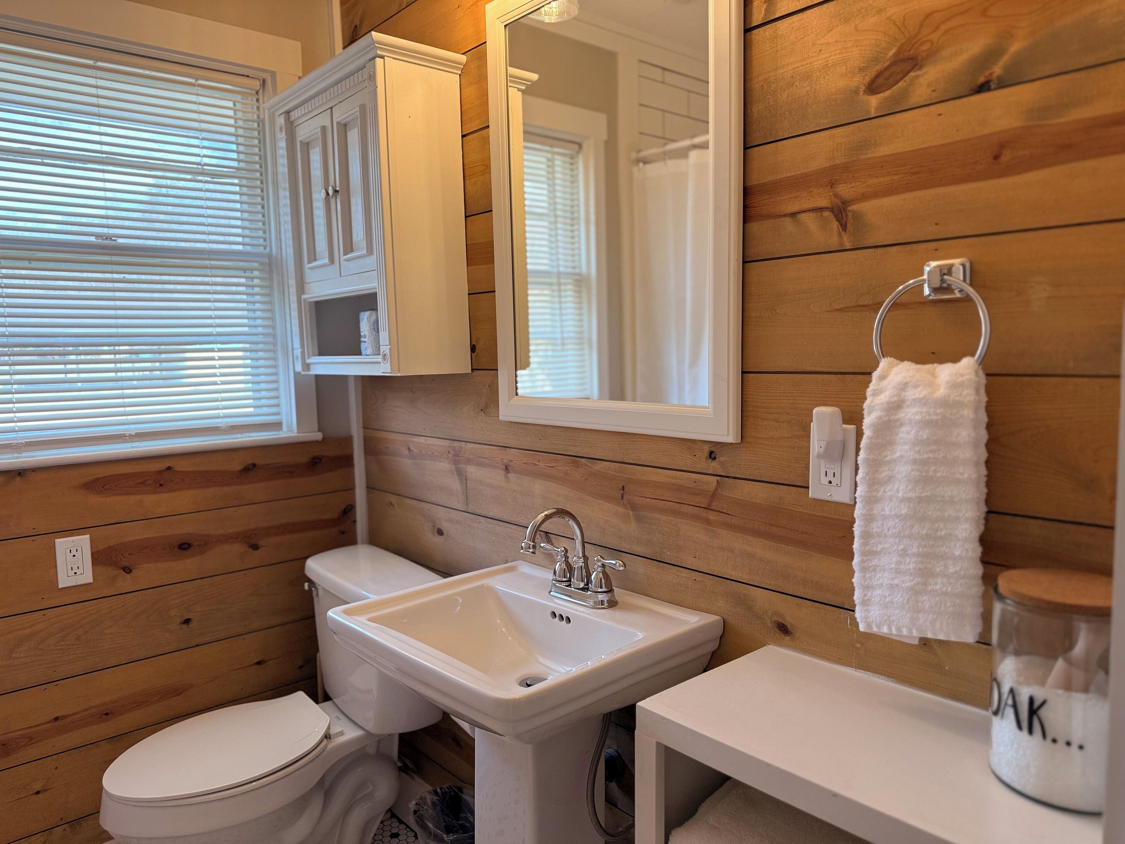 Un bagno con rivestimenti in legno, un WC bianco, un lavabo con specchio sopra e un asciugamano appeso a un supporto.