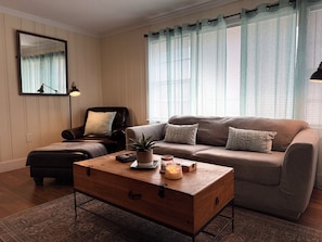 A living room with a sofa, a chair, a wooden coffee table, and a mirror on the wall.