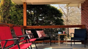 A covered patio area with red and black chairs, a small table, and a rug. - Lazy Hiker by Chatuge Home Concierge | Walk to Downtown Hayesville | Fire Pit | Pet Friendly (Hayesville)