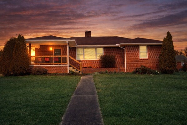 A two-story brick house with a front porch, a covered patio, and a well-maintained lawn.