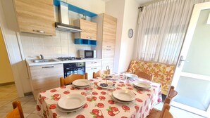 Eine kompakte Küche mit modernen Geräten, ein Essbereich mit Tisch für vier Personen und ein Sofa mit Blumenmuster.