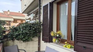 A balcony with two grey chairs, a window with brown shutters, and a vase with yellow flowers. - Three-room apartment Nicole with private garden Elba Island (Porto Azzurro)