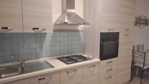 A modern kitchen with light-colored cabinets, a gas stove, an oven, and a blue-tiled backsplash. - Three-room apartment Nicole with private garden Elba Island (Porto Azzurro)