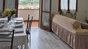 A room with a dining table set for four, a sofa, and a view of a mountainous landscape through a large sliding glass door. - Three-room apartment Nicole with private garden Elba Island (Porto Azzurro)