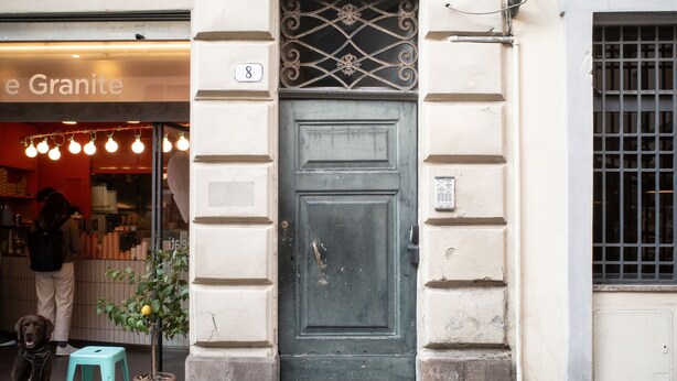 A building entrance with a green door, a small potted plant, and a teal stool. - Charming Apartment in the Historic Center (Lucca)