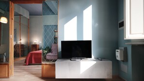 A modern living room with a flat-screen TV on a white console, a pink chair, and a wooden cabinet. - Charming Apartment in the Historic Center (Lucca)