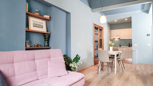 A modern living room with a pink sofa, wooden flooring, and a dining area with a table and chairs. - Charming Apartment in the Historic Center (Lucca)