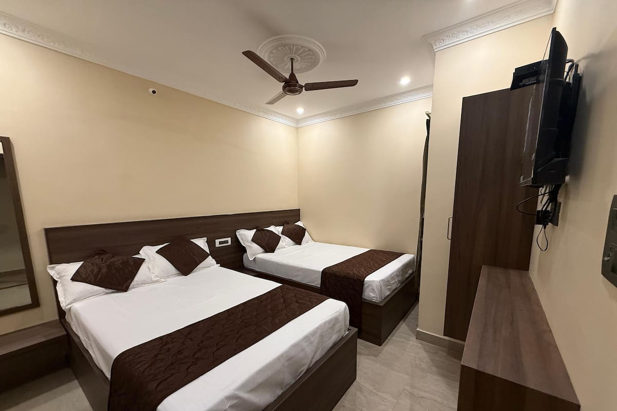 A hotel room with two beds, a ceiling fan, a TV mounted on the wall, and a wooden wardrobe.