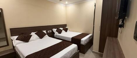 Habitación de hotel con dos camas, ventilador de techo, televisor montado en la pared y armario de madera.