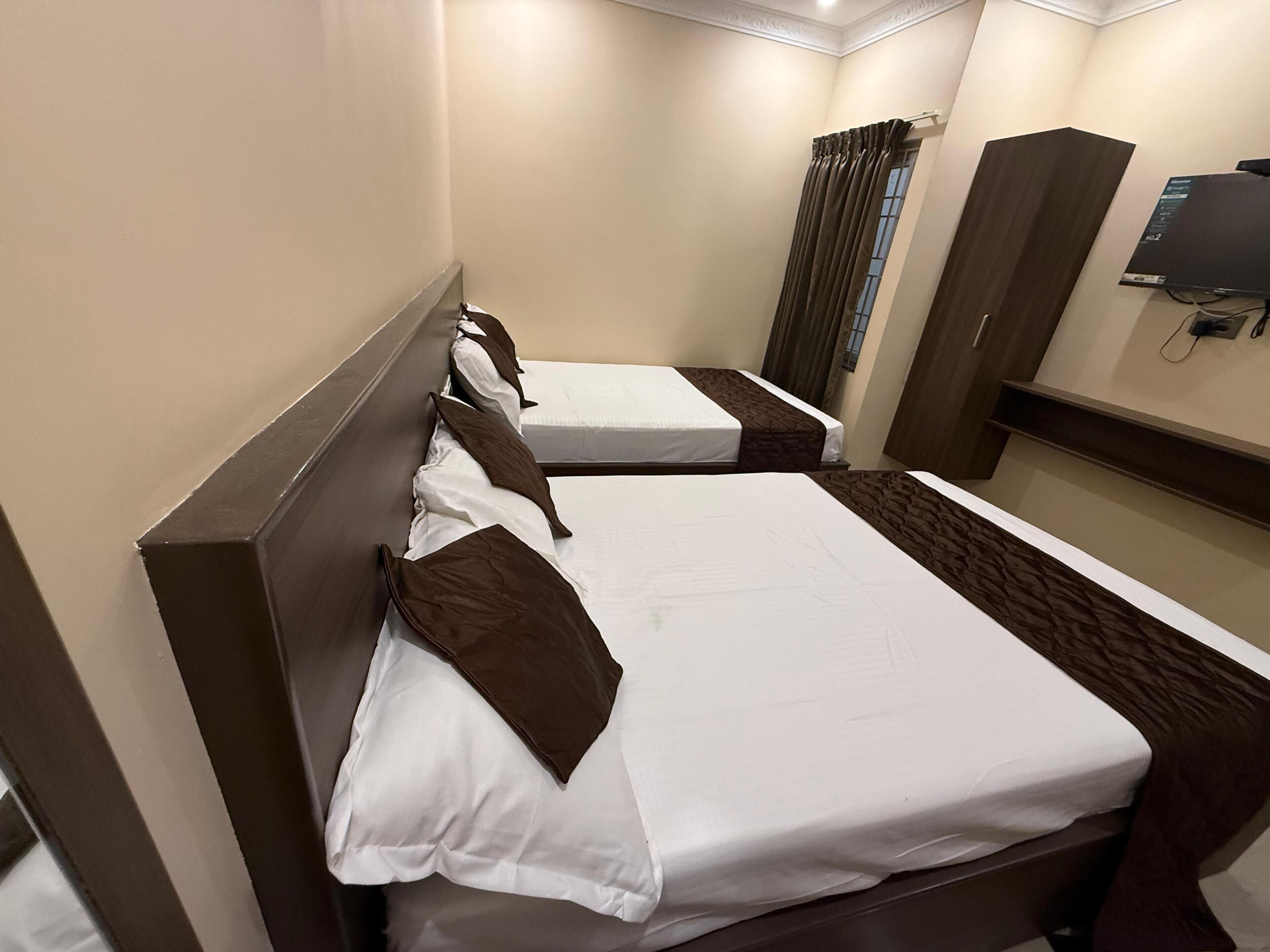 A hotel room with two single beds, a wardrobe, a television, and a window with curtains.