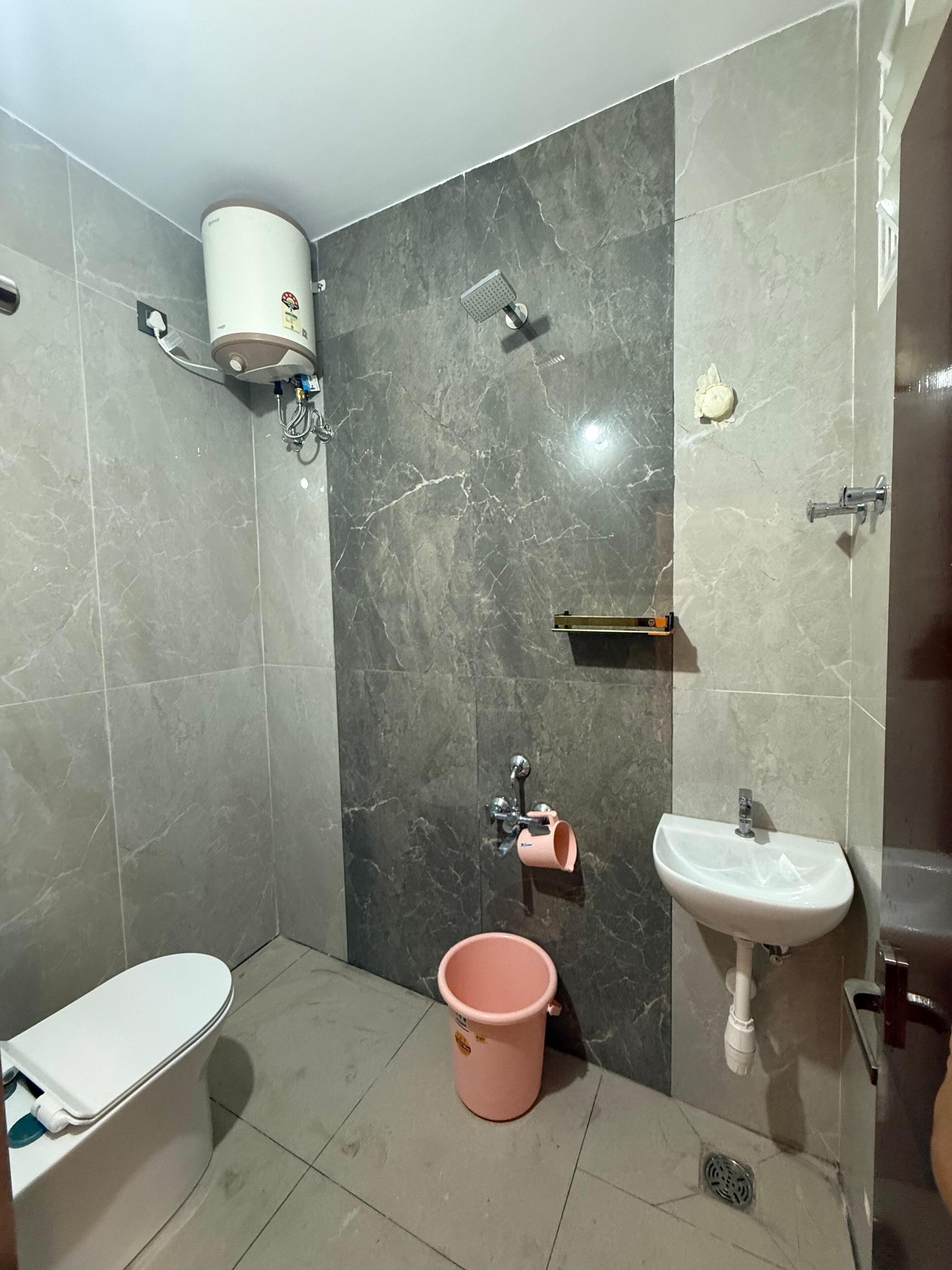 A bathroom with a toilet, a sink, a shower, and a bucket.