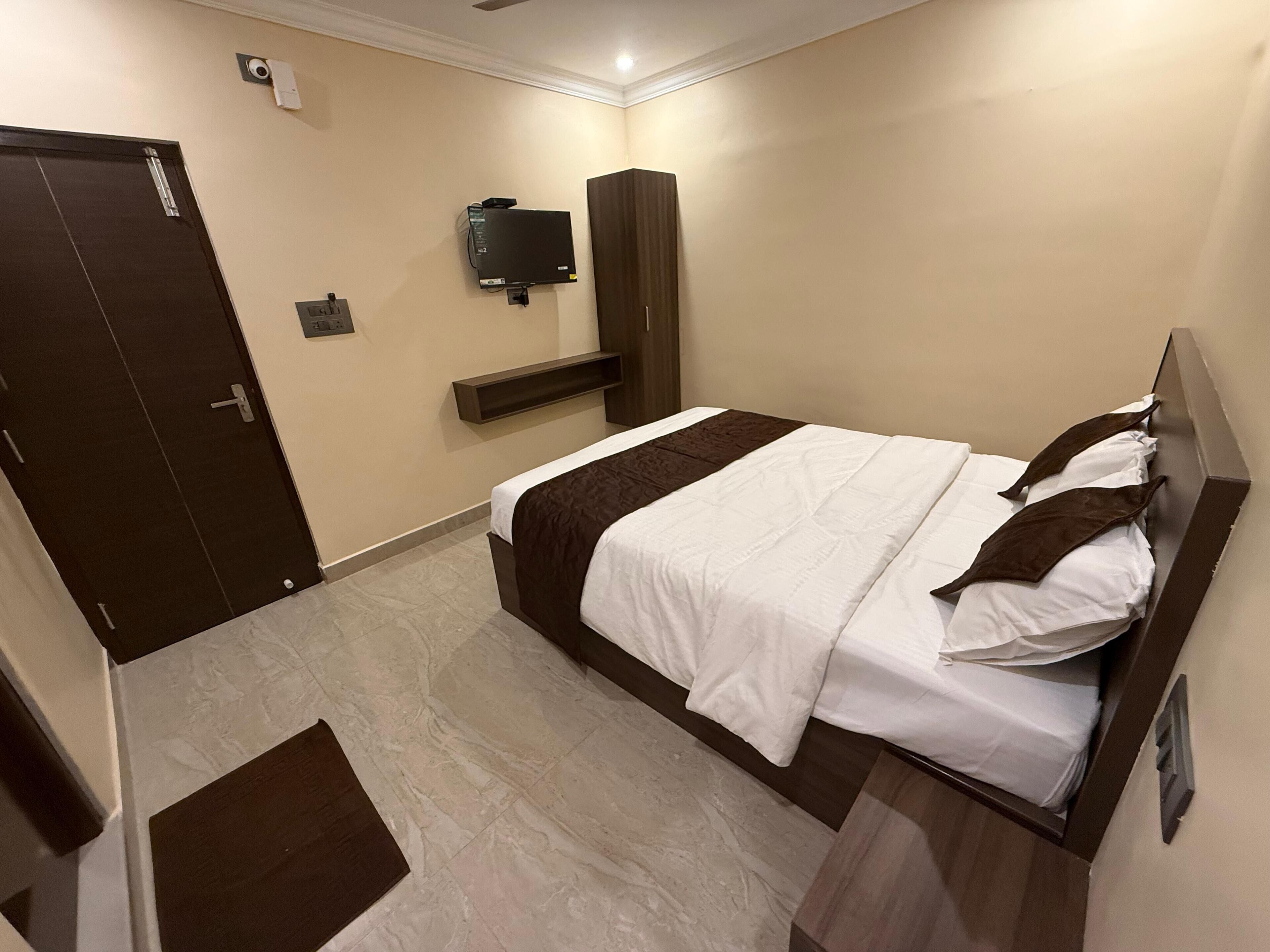 A hotel room with a bed, a TV mounted on the wall, a door, and a small shelf.