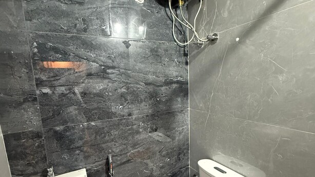A bathroom with a black marble wall, a white sink, a toilet, and a shower unit. - Ragha Residency (Kanchipuram)