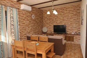 A cozy living room with a wooden dining table, sofa, and TV. - Casa Elena Conil   . (Conil de la Frontera)