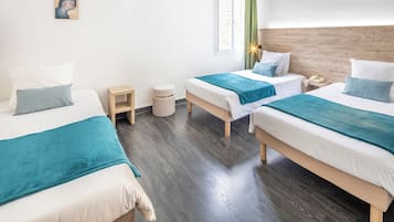 Habitación de hotel con tres camas, un taburete de madera, un otomano redondo y un cuadro en la pared.