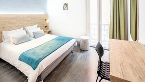 Ein Hotelzimmer mit Bett, einem kleinen Tisch, einem Sessel, einem runden Hocker und einem Fenster mit Vorhängen.