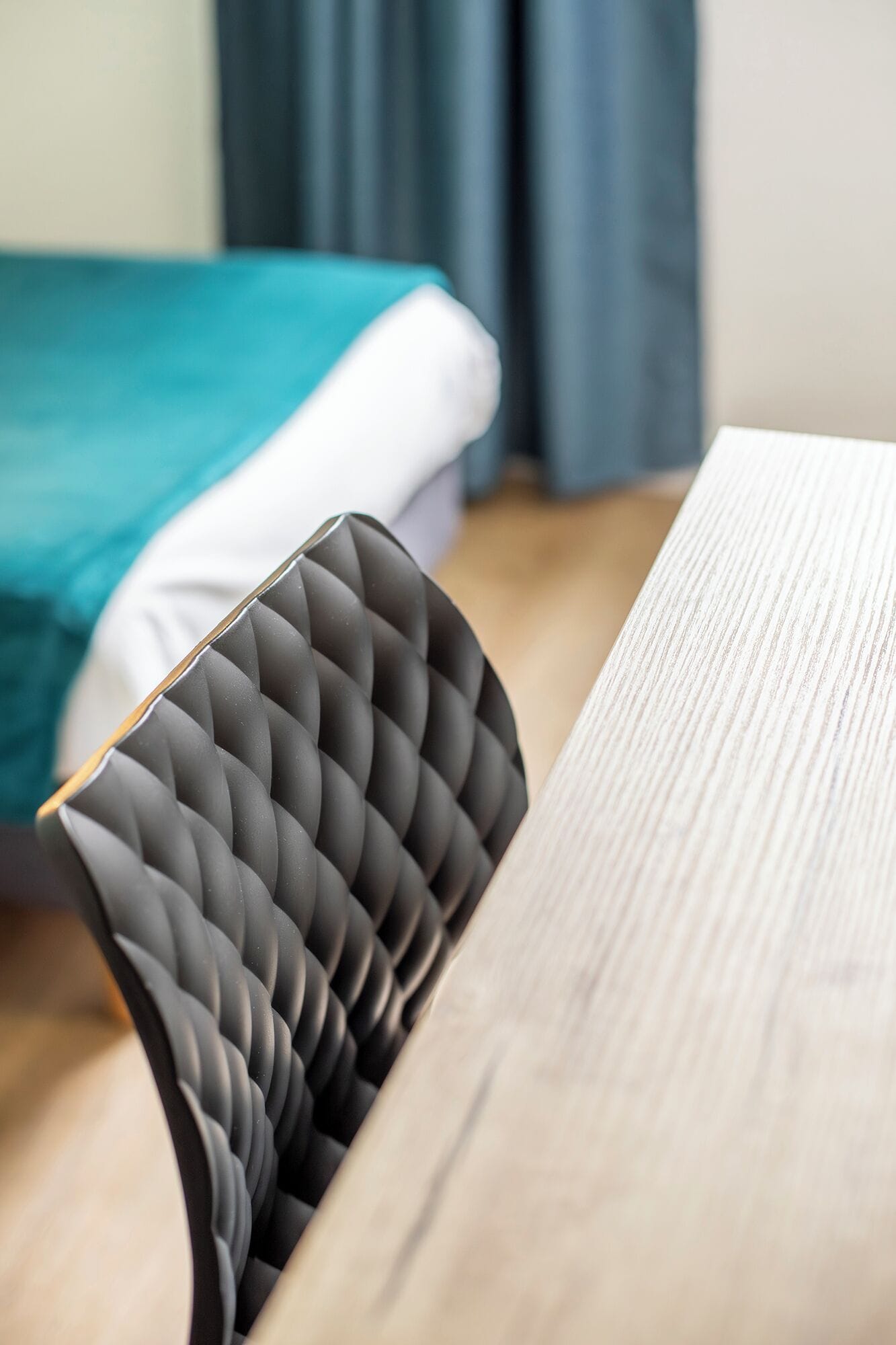 Una habitación moderna con cama, una mesa de madera y una silla tapizada de color negro.