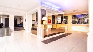 Eine moderne Hotelhalle mit einer Rezeption, einer Sitzecke und einer Treppe zu den oberen Etagen.