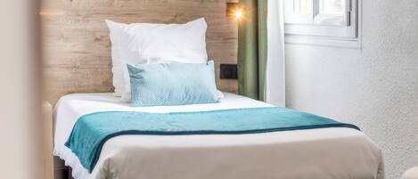 A neatly made bed with a wooden headboard, a green curtain, and a window with daylight.