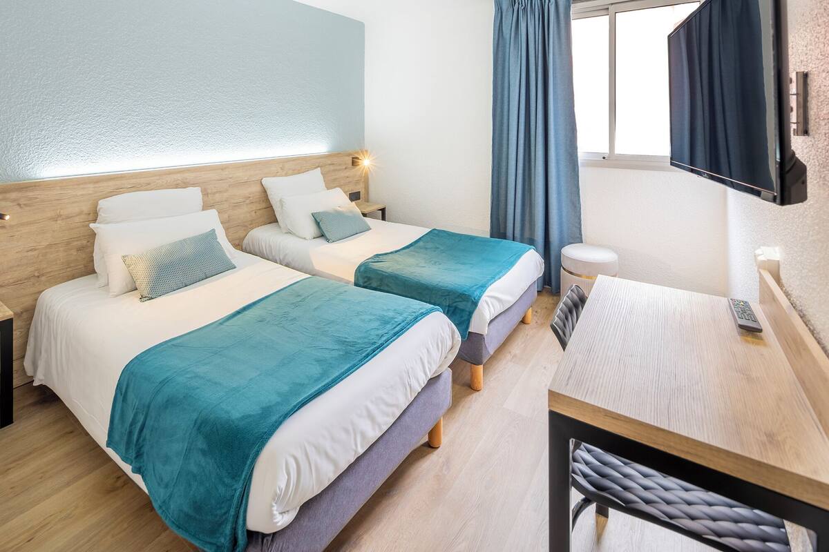 Une chambre d’hôtel avec deux lits, un bureau, une télévision et une fenêtre avec des rideaux.