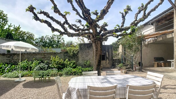 A patio with a table and chairs, surrounded by gravel, a tree, and potted plants.