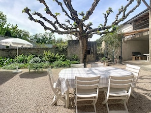 A patio with a table and chairs, surrounded by gravel, a tree, and potted plants. - Gîte Fleurs de Gamay, in the heart of the Beaujolais region. Pets allowed (Lancié)