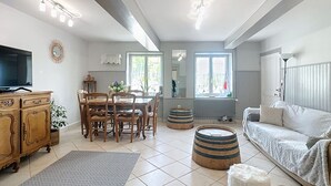 A spacious living area with a dining table, chairs, a sofa, a television, and a large window.