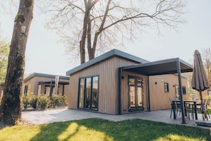 A modern building with a covered patio area, large windows, and a grassy lawn.