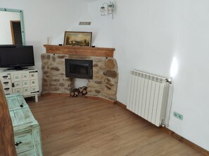 Una sala de estar con chimenea de piedra, un televisor sobre un mueble bajo y un radiador blanco.