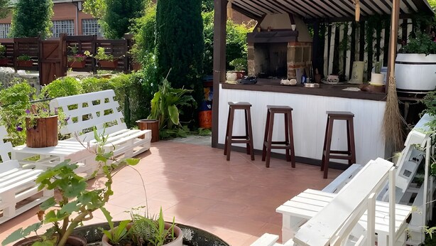 Eine Außenpatio mit Grillplatz, weißen Lounge-Stühlen und Topfpflanzen.