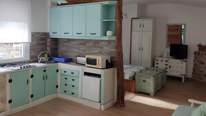 Eine kompakte Küche mit Gasherd, Mikrowelle und Spüle. Eine Holzbalkenkonstruktion befindet sich über den Schränken, und ein Fernseher ist an der Wand montiert.