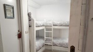 Una habitación con literas, una escalera de caracol, una puerta con candado y un cuadro en la pared.
