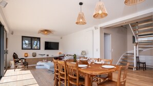 A dining area with a wooden table and chairs, a TV mounted on the wall, and a staircase leading to an upper level. - Maison Desmathi: terrace with jacuzzi, garden, in Saint-Pierre-Quiberon (Saint-Pierre-Quiberon)